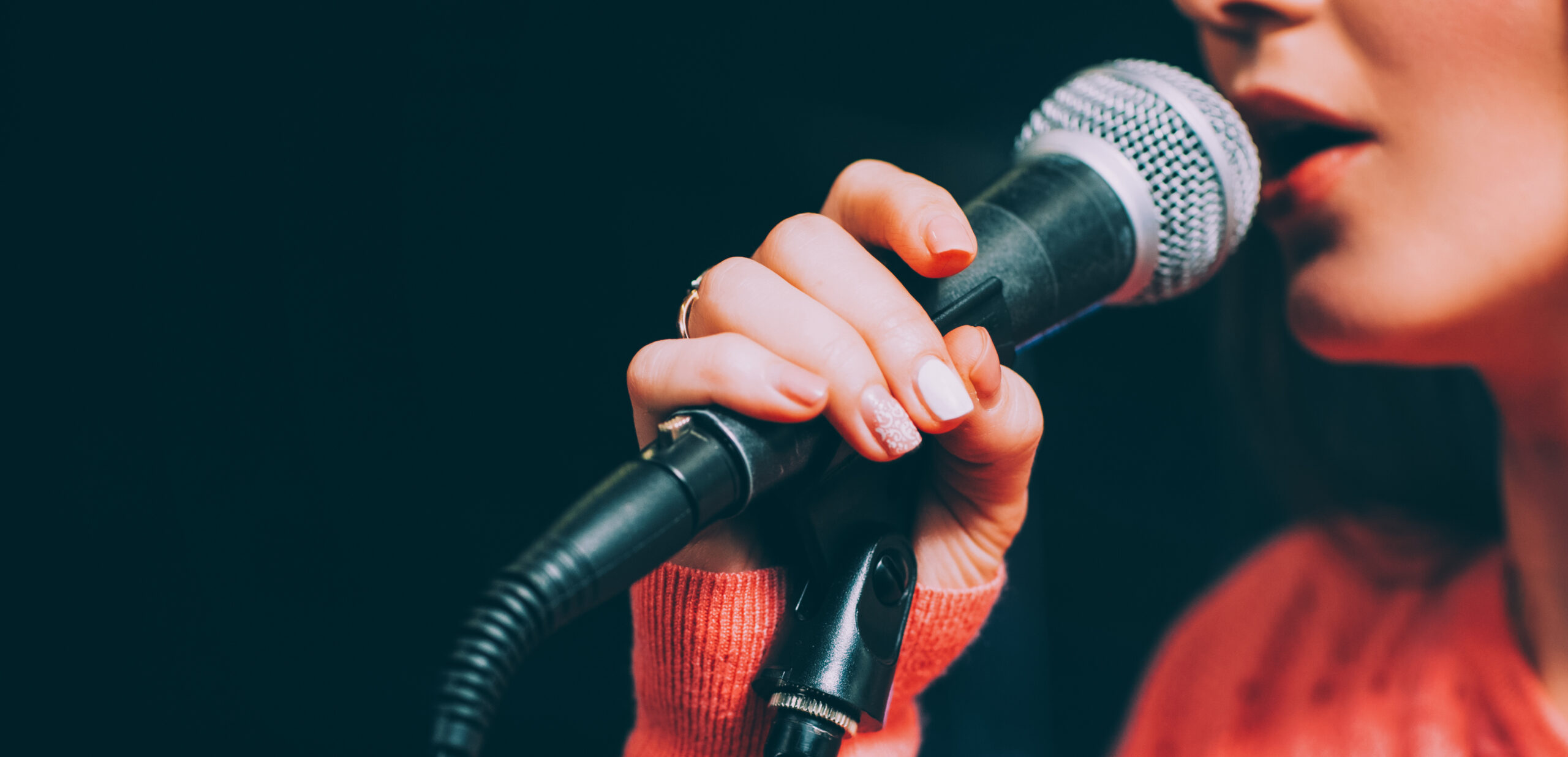 Singer at microphone. Woman singing and holding mic. Female vocal talent. Music show recital.