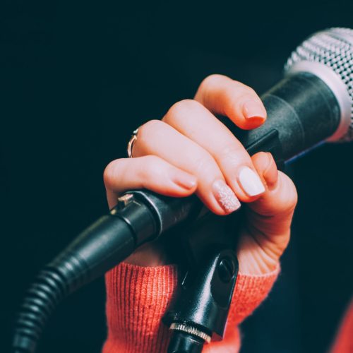 Singer at microphone. Woman singing and holding mic. Female vocal talent. Music show recital.